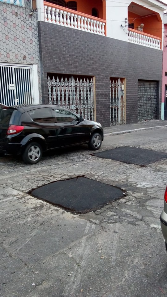 Dois buracos tapados na rua; ao fundo, um carro preto estacionado.